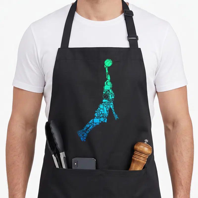 Dunking basketball apron - Jumping player silhouette formed by green and blue basketball icons in minimalist collage — shown on a black cotton canvas apron against a white background