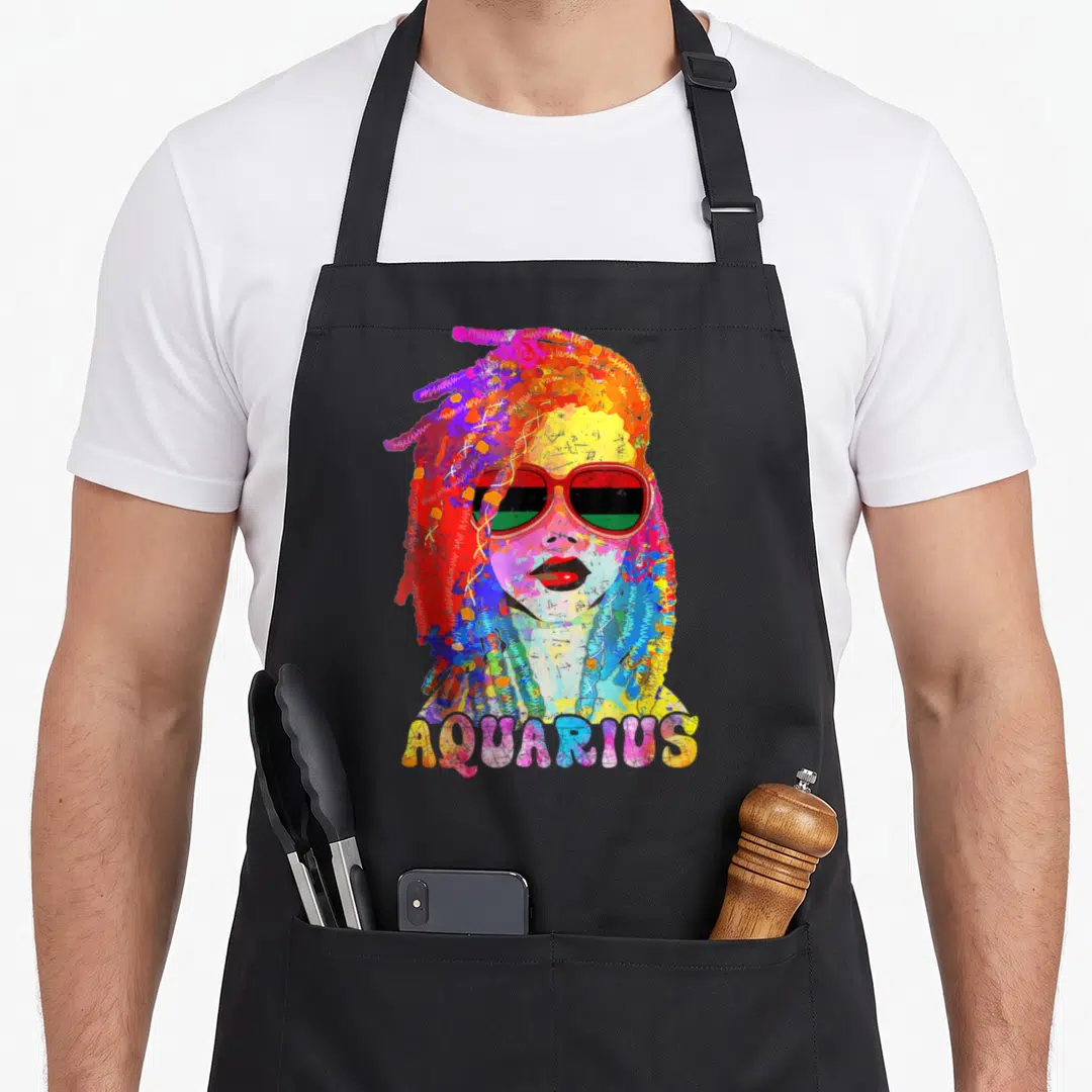 Zodiac hair apron - Watercolor woman with dreadlocks and red sunglasses, AQUARIUS text below in multicolor letters — shown on a black cotton canvas apron against a white background