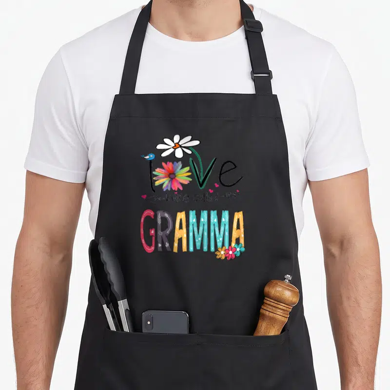 Gramma mother's day aprons - Love being called GRAMMA text with bird, flowers, and arrows in pink, blue, orange — shown on a black cotton canvas apron against a white background