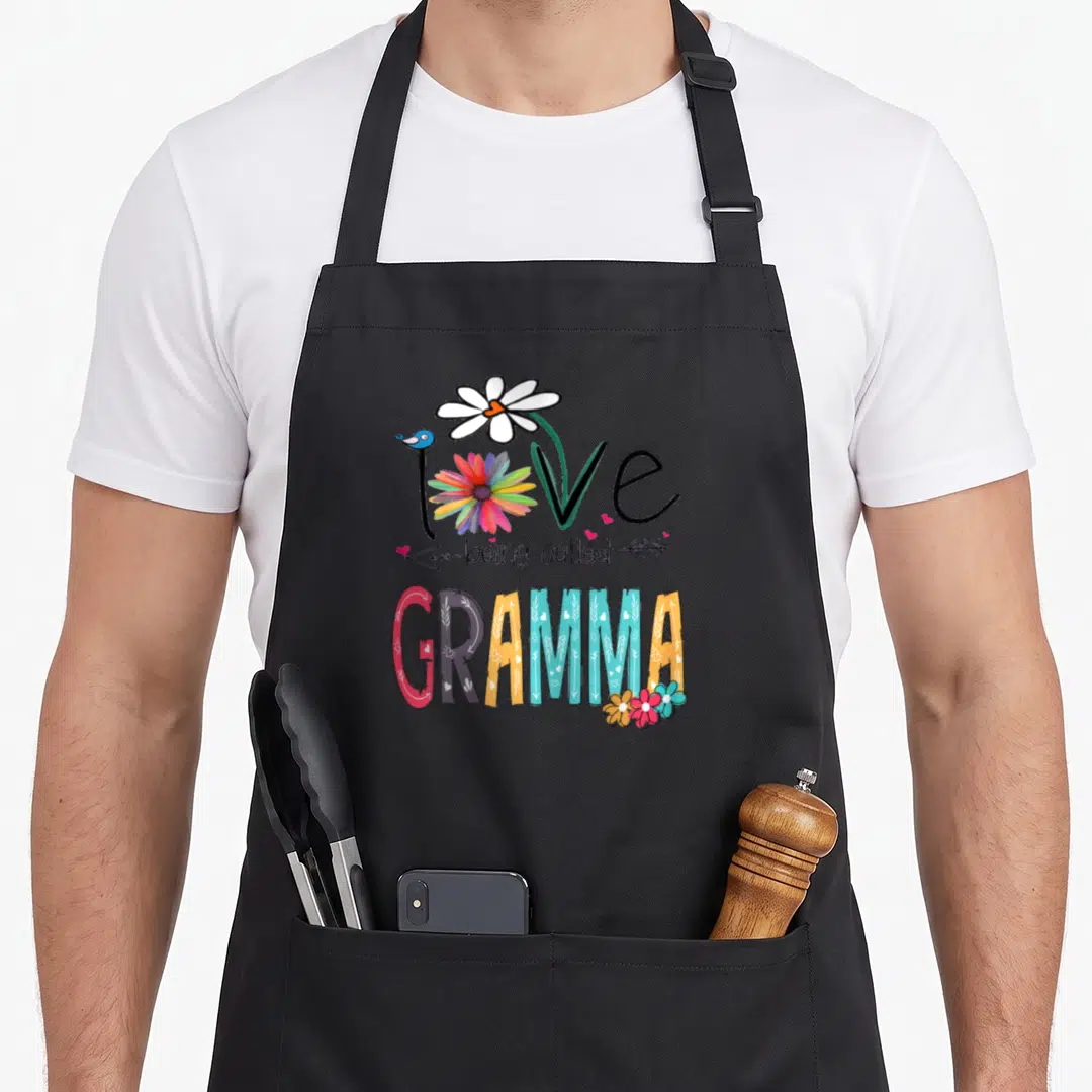 Gramma mother's day aprons - Love being called GRAMMA text with bird, flowers, and arrows in pink, blue, orange — shown on a black cotton canvas apron against a white background