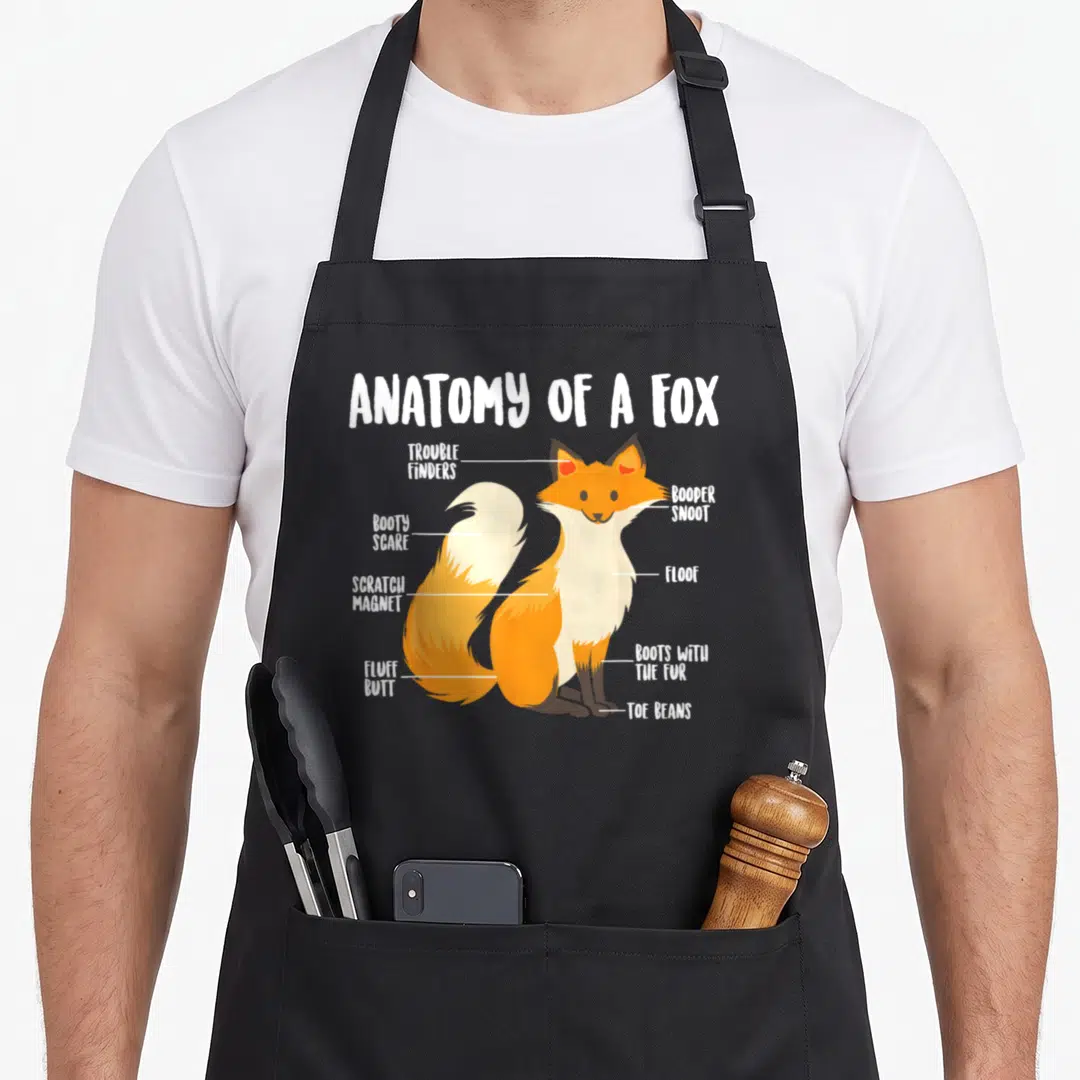 Fox anatomy apron - Cartoon fox diagram labeled with funny body part names like Booty Scare and Toe Beans — shown on a black cotton canvas apron against a white background