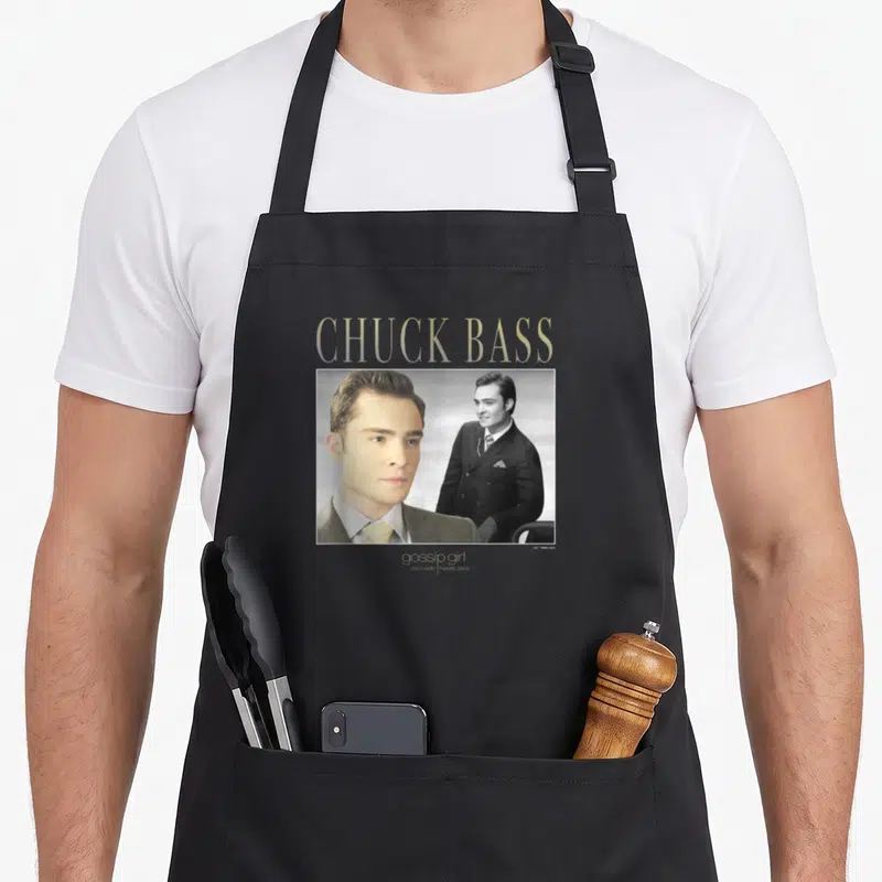 Chuck gossip apron - Gold CHUCK BASS text above photo of man in suit with gossip girl tagline — shown on a black cotton canvas apron against a white background