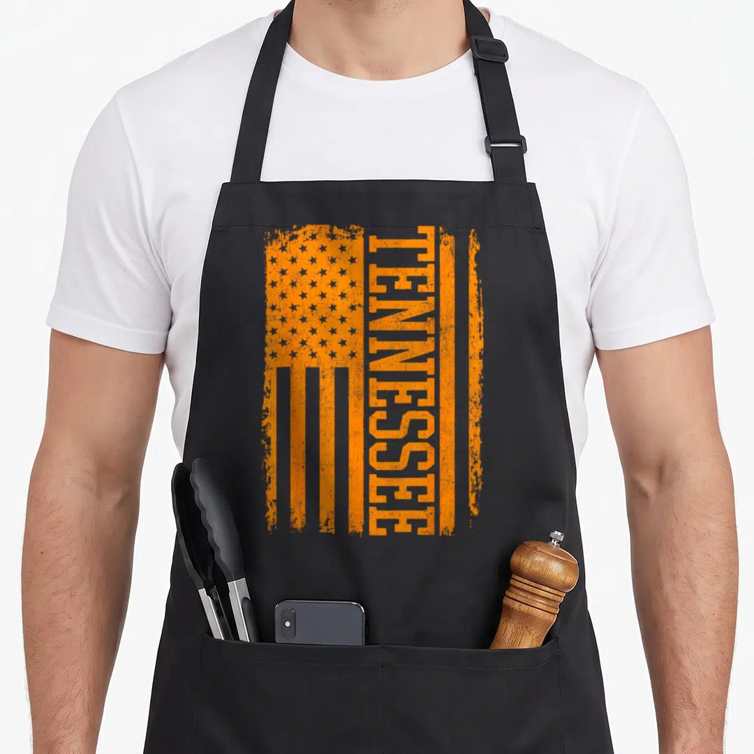 Varsity tennessee river apron - Vertical orange TENNESSEE text forming stripes in a distressed USA flag pattern — shown on a black cotton canvas apron against a white background