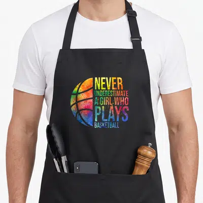 Hoop indiana fever apron - Colorful watercolor basketball with stacked text Never Underestimate A Girl Who Plays — shown on a black cotton canvas apron against a white background