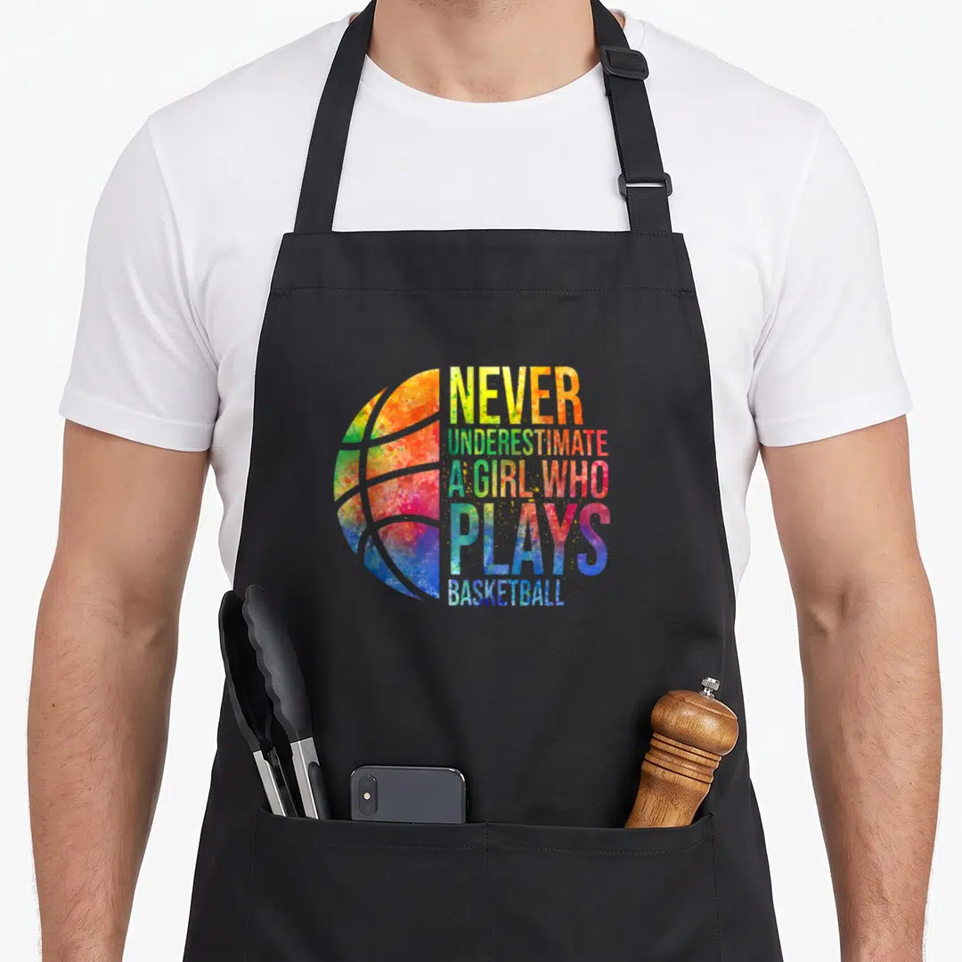 Hoop indiana fever apron - Colorful watercolor basketball with stacked text Never Underestimate A Girl Who Plays — shown on a black cotton canvas apron against a white background