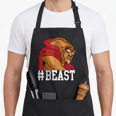 Beast face apron - Cartoon beast in red cape with white #BEAST text at bottom — shown on a black cotton canvas apron against a white background