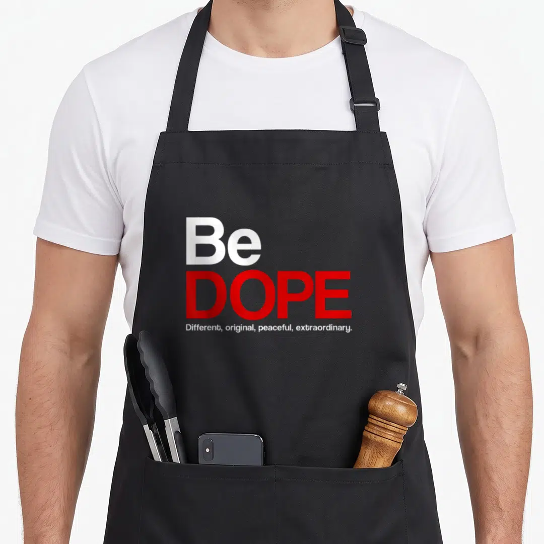 Dope special husband apron - Red and white stacked text Be DOPE Different original peaceful extraordinary on black — shown on a black cotton canvas apron against a white background