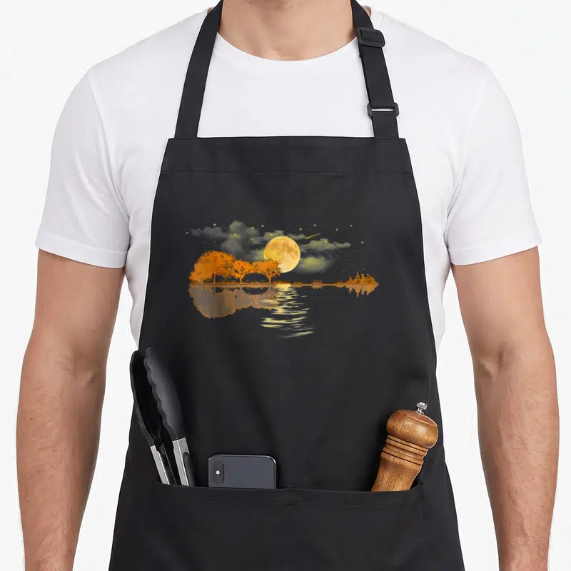 Guitar vintage nature apron - Orange trees and grey city skyline reflected under a yellow moon on water — shown on a black cotton canvas apron against a white background