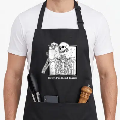 Baby goth apron - White line-art skeleton holding a drink inside a black frame with text below — shown on a black cotton canvas apron against a white background