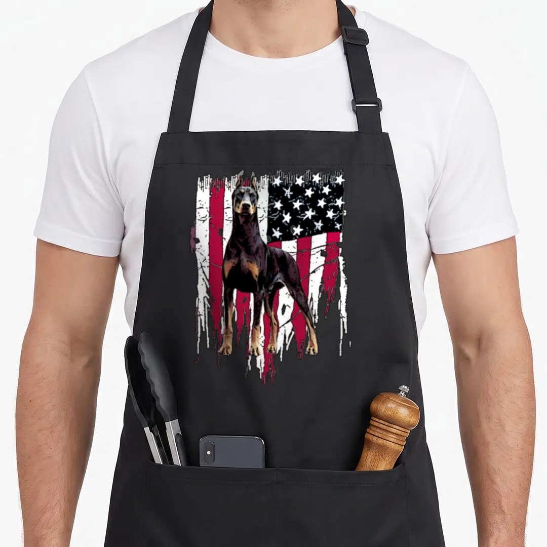 Doberman pinscher american flag apron - Black doberman standing before a dripping distressed red white and blue flag — shown on a black cotton canvas apron against a white background