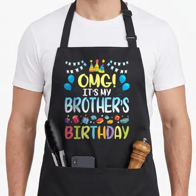 Cousin birthday apron - OMG It's My Brothers Birthday text with cartoon hats, balloons, bunting, and gifts in yellow — shown on a black cotton canvas apron against a white background