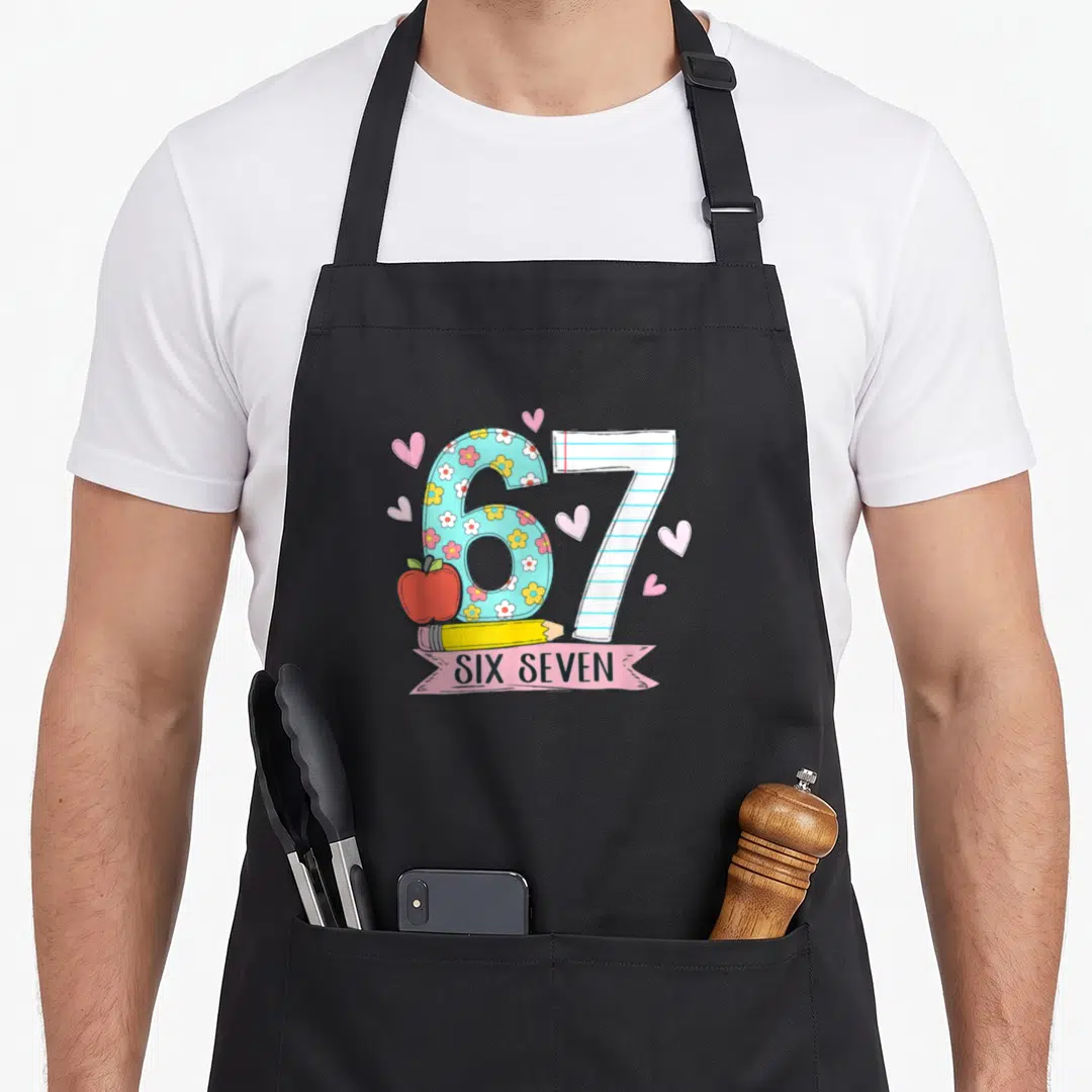 Six teacher apron - Cartoon 67 with floral six, lined seven, red apple, yellow pencil, and hearts — shown on a black cotton canvas apron against a white background