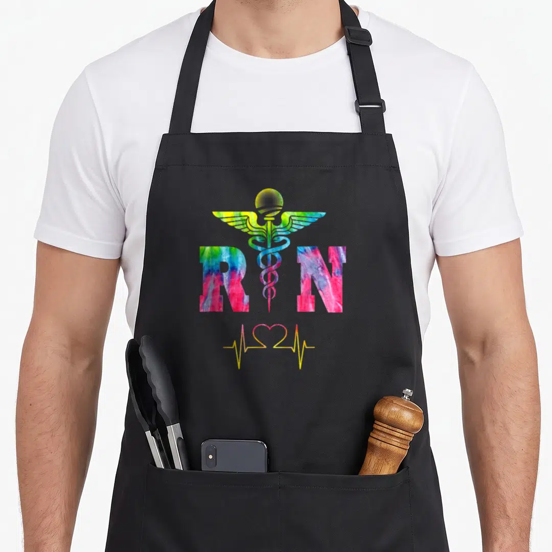 Registered professional apron - Tie-dye RN letters with caduceus and heartbeat line graphic — shown on a black cotton canvas apron against a white background
