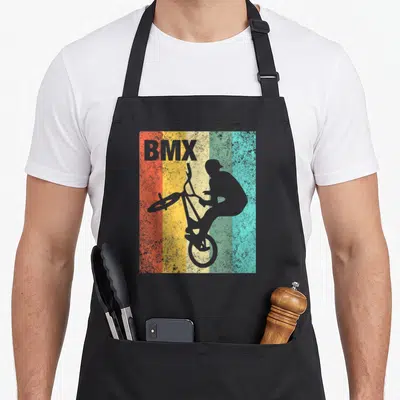 Bmx bicycle apron - Grey BMX rider silhouette over orange yellow green blue and grey vertical stripes — shown on a black cotton canvas apron against a white background