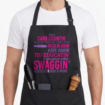 T1d diabetic diabetes awareness apron - Pink and purple text reading I'm a carb countin d-mom with syringe icon — shown on a black cotton canvas apron against a white background