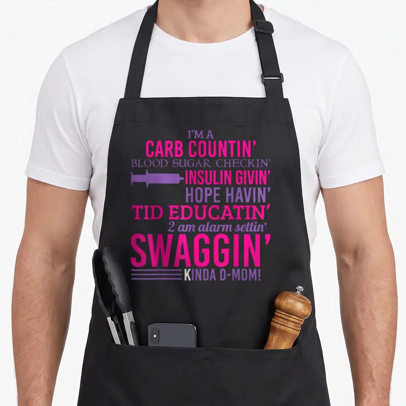 T1d diabetic diabetes awareness apron - Pink and purple text reading I'm a carb countin d-mom with syringe icon — shown on a black cotton canvas apron against a white background