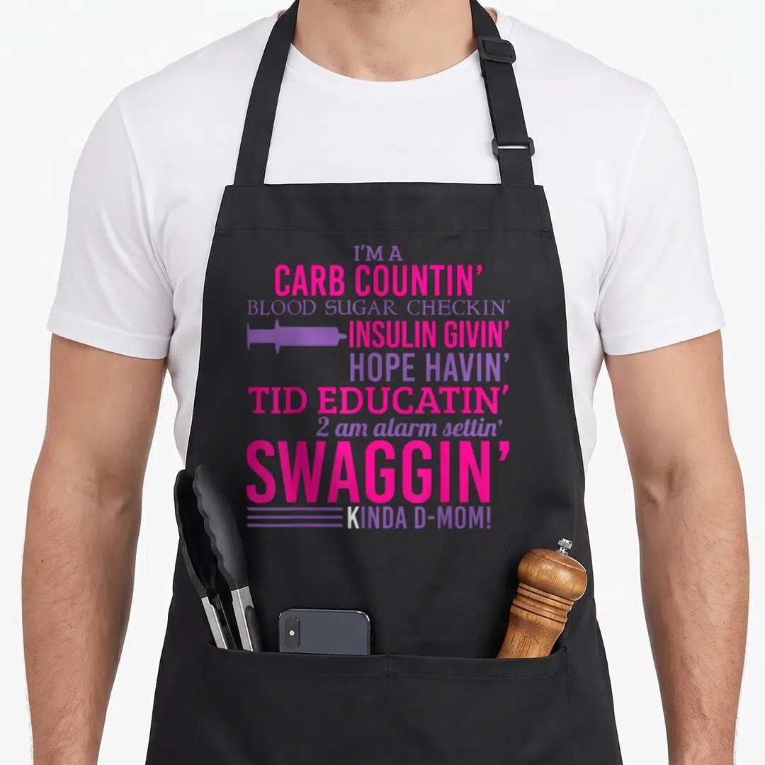 T1d diabetic diabetes awareness apron - Pink and purple text reading I'm a carb countin d-mom with syringe icon — shown on a black cotton canvas apron against a white background