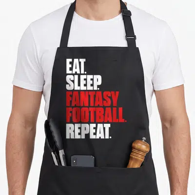 Eat sleep football apron - Stacked white and red text reading EAT SLEEP FANTASY FOOTBALL REPEAT on black fabric — shown on a black cotton canvas apron against a white background