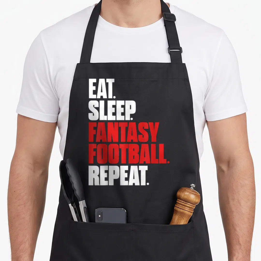 Eat sleep football apron - Stacked white and red text reading EAT SLEEP FANTASY FOOTBALL REPEAT on black fabric — shown on a black cotton canvas apron against a white background