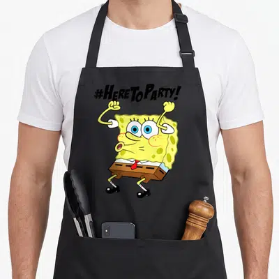 Funny squarepant novelty apron - SpongeBob with raised arms under '#HERE TO PARTY!' text in yellow brown and red — shown on a black cotton canvas apron against a white background