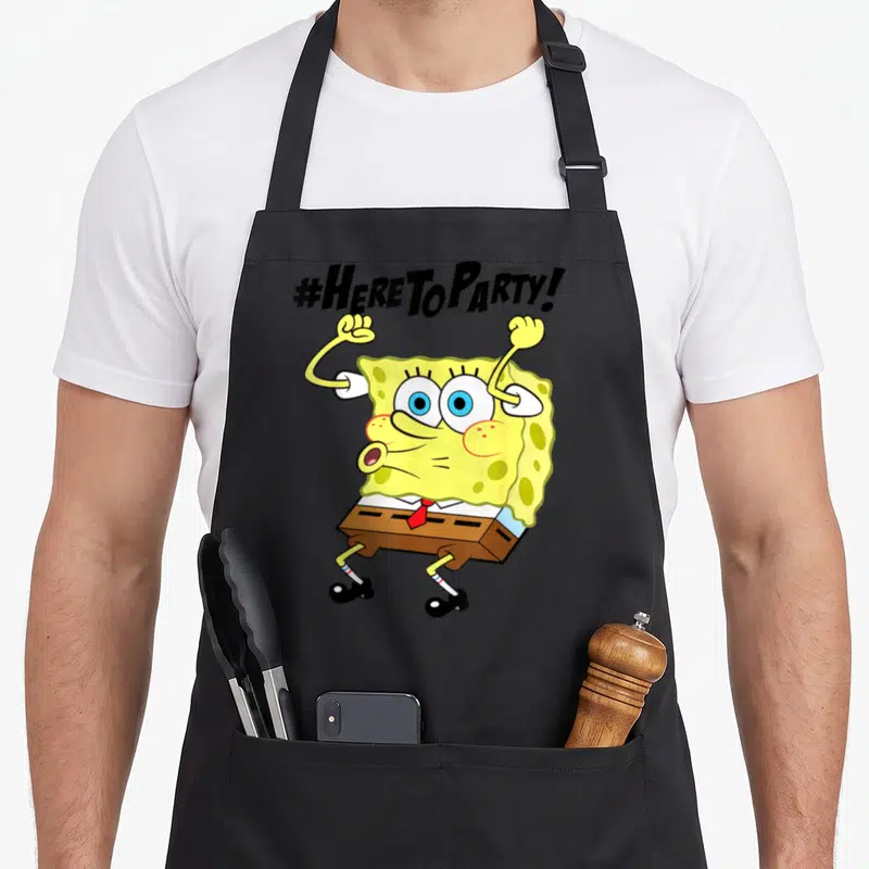 Funny squarepant novelty apron - SpongeBob with raised arms under '#HERE TO PARTY!' text in yellow brown and red — shown on a black cotton canvas apron against a white background