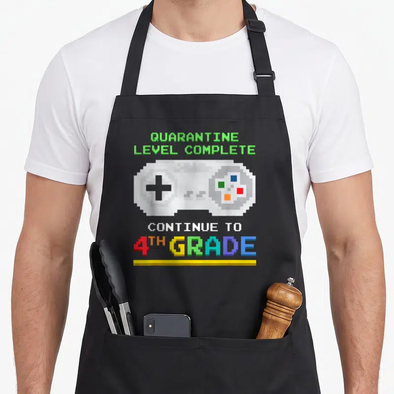 Level quarantine aprons - Pixel game controller with QUARANTINE LEVEL COMPLETE and 4TH GRADE text in rainbow colors — shown on a black cotton canvas apron against a white background
