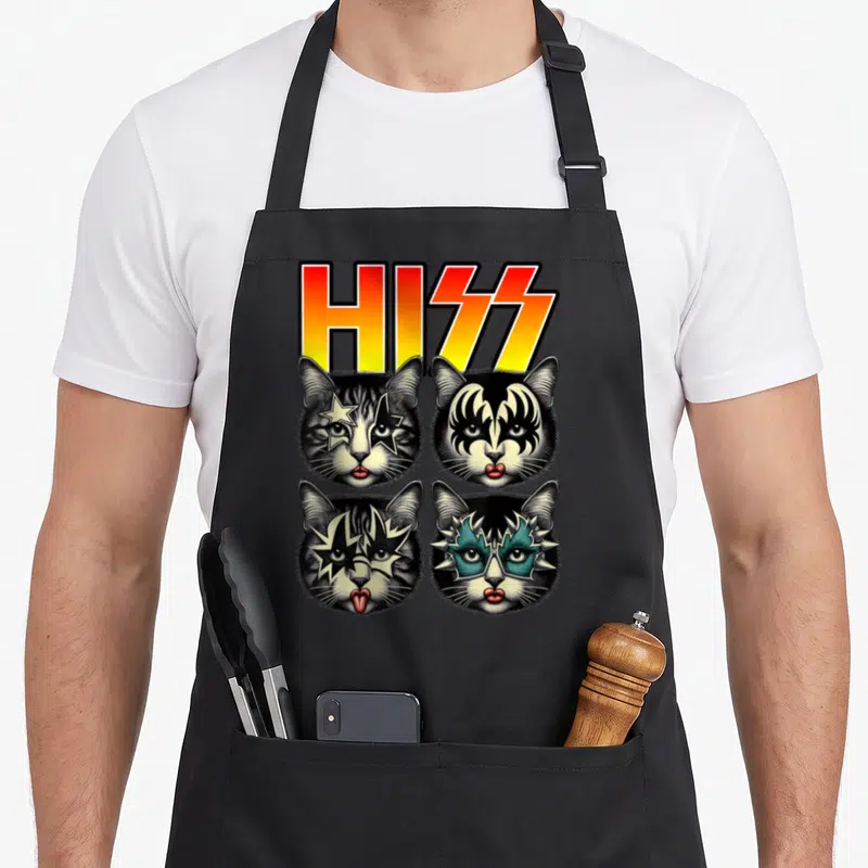 Hiss cat apron - Four cartoon cats with rock face paint under red yellow HISS text — shown on a black cotton canvas apron against a white background