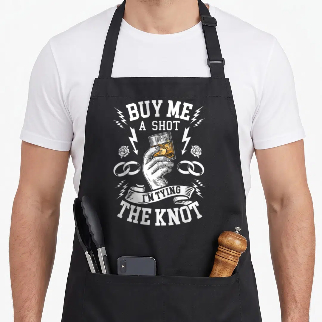 Groomsmen groom apron - Hand holding orange shot glass flanked by white rings and lightning bolts — shown on a black cotton canvas apron against a white background