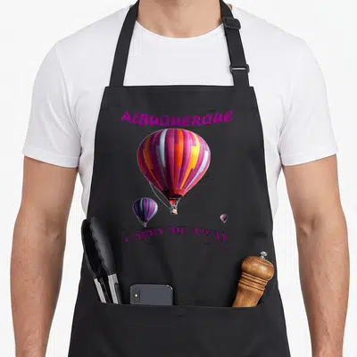 Albuquerque balloon apron - Colorful hot air balloon photo with purple text Albuquerque and Carry Me Away script — shown on a black cotton canvas apron against a white background