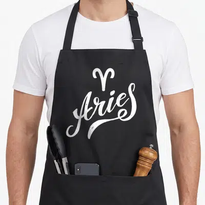 Funny zodiac aries kitchen apron - White Aries zodiac symbol and script text on dark background — shown on a black cotton canvas apron against a white background