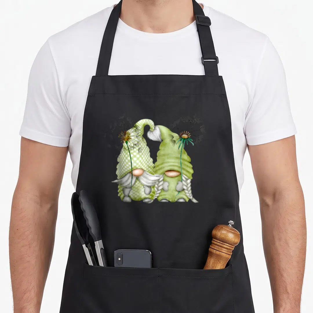 Dandelion gnome apron - Two gnomes with dandelion seed heads on hats in green watercolor style — shown on a black cotton canvas apron against a white background