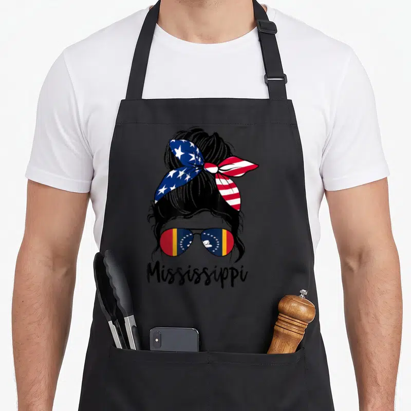 Flag mississippi girl apron - Cartoon woman with US headband and Mississippi flag sunglasses above printed text — shown on a black cotton canvas apron against a white background