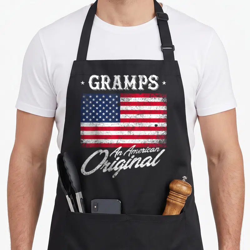 Gramp 4th of july apron - Distressed USA flag with GRAMPS text and An American Original slogan in white red and blue — shown on a black cotton canvas apron against a white background