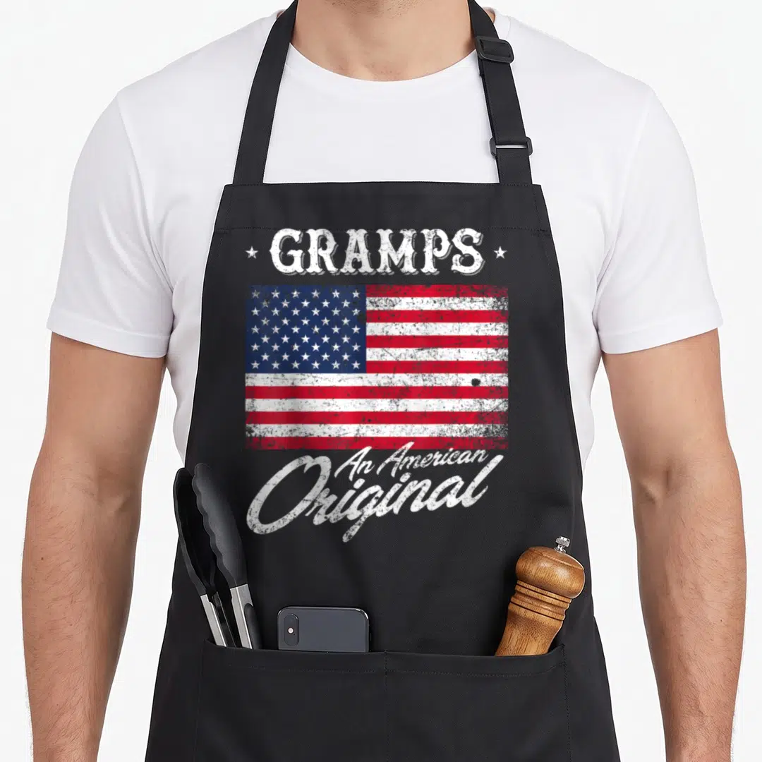 Gramp 4th of july apron - Distressed USA flag with GRAMPS text and An American Original slogan in white red and blue — shown on a black cotton canvas apron against a white background