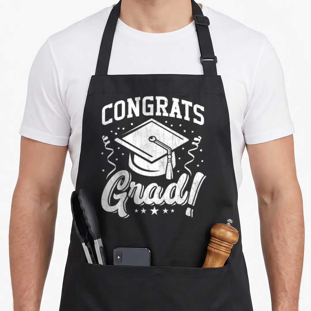 Graduate congrats apron - White distressed graduation cap with CONGRATS Grad text and stars — shown on a black cotton canvas apron against a white background