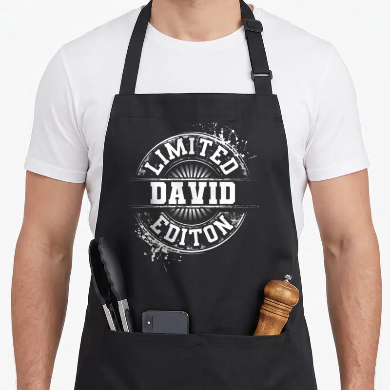 David family reunion aprons - White distressed circular stamp reading LIMITED DAVID EDITON with paint splatters — shown on a black cotton canvas apron against a white background