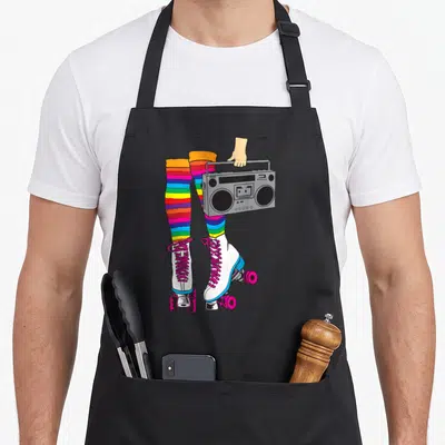 Rollerskate 80s apron - Cartoon legs in rainbow striped socks and white roller skates holding a grey boombox — shown on a black cotton canvas apron against a white background
