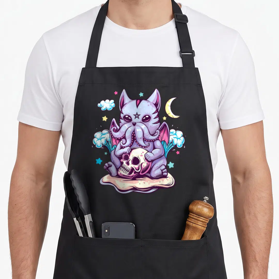 Creature goth apron - Purple cthulhu cat with wings holding skull surrounded by pastel moon stars and splashing water — shown on a black cotton canvas apron against a white background