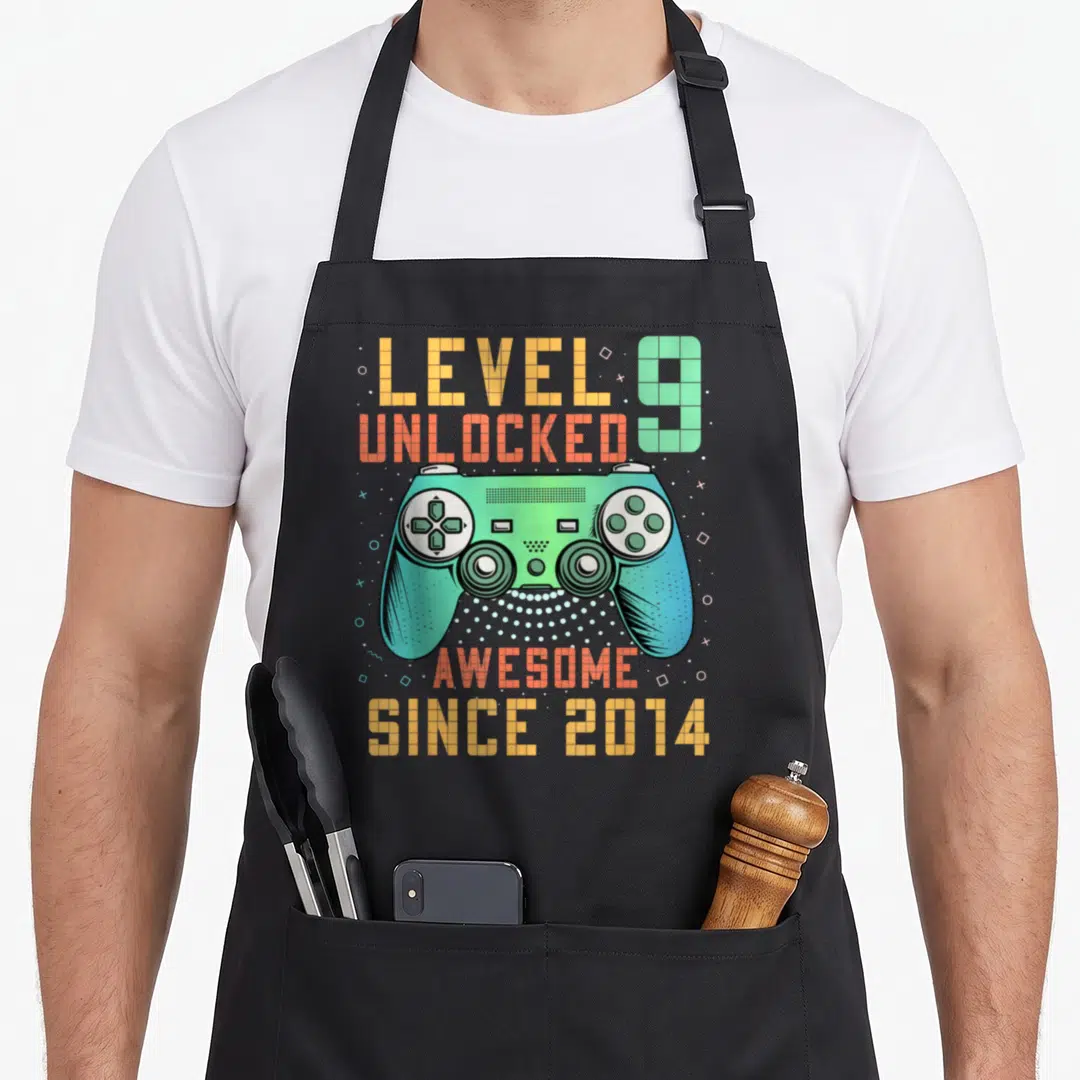 Level unlocked 9th birthday apron - Teal game controller with LEVEL 9 UNLOCKED and AWESOME SINCE 2014 text in retro — shown on a black cotton canvas apron against a white background