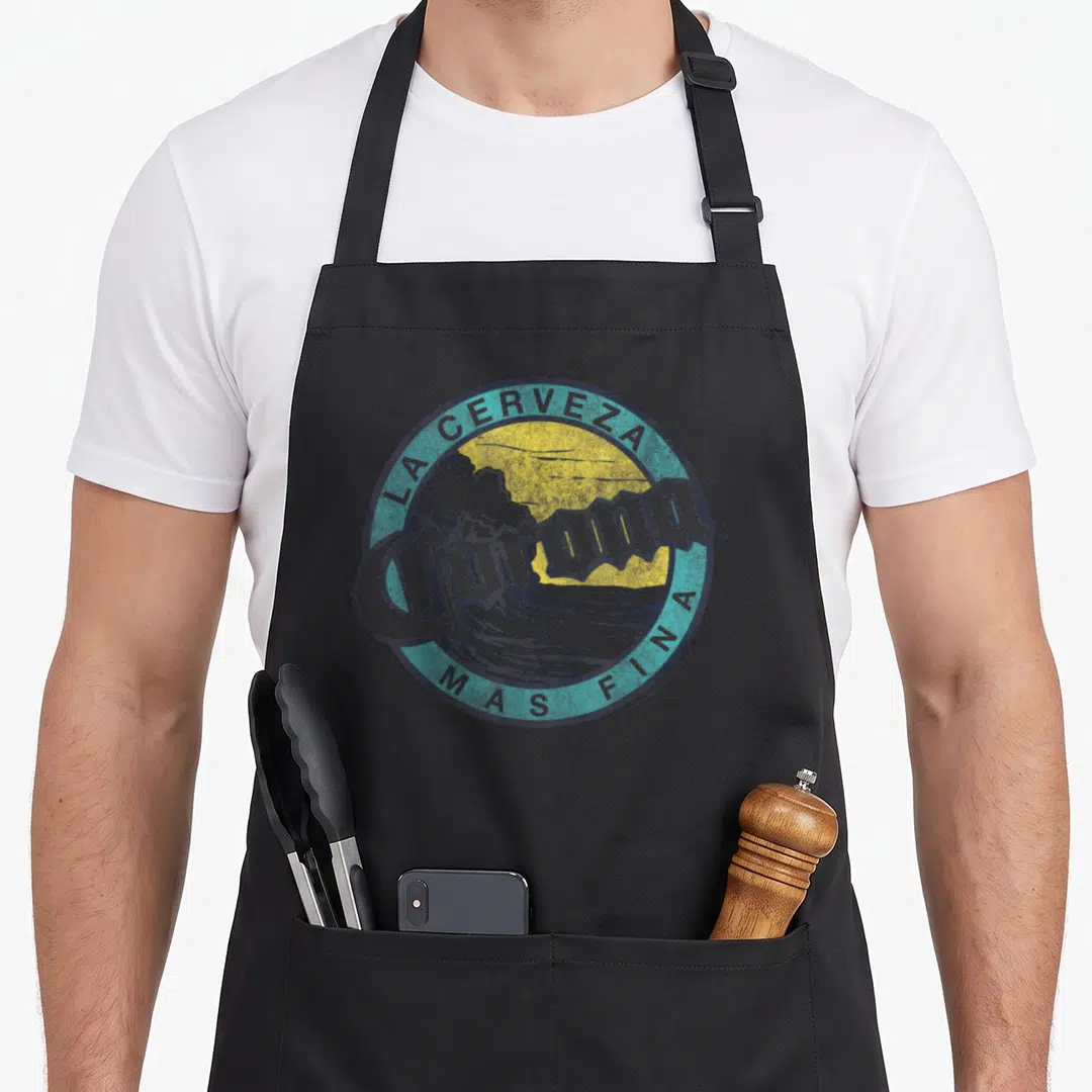 Corona best class ever apron - Retro circular logo with yellow sun, teal border reading LA CERVEZA MAS FINA, and grey — shown on a black cotton canvas apron against a white background