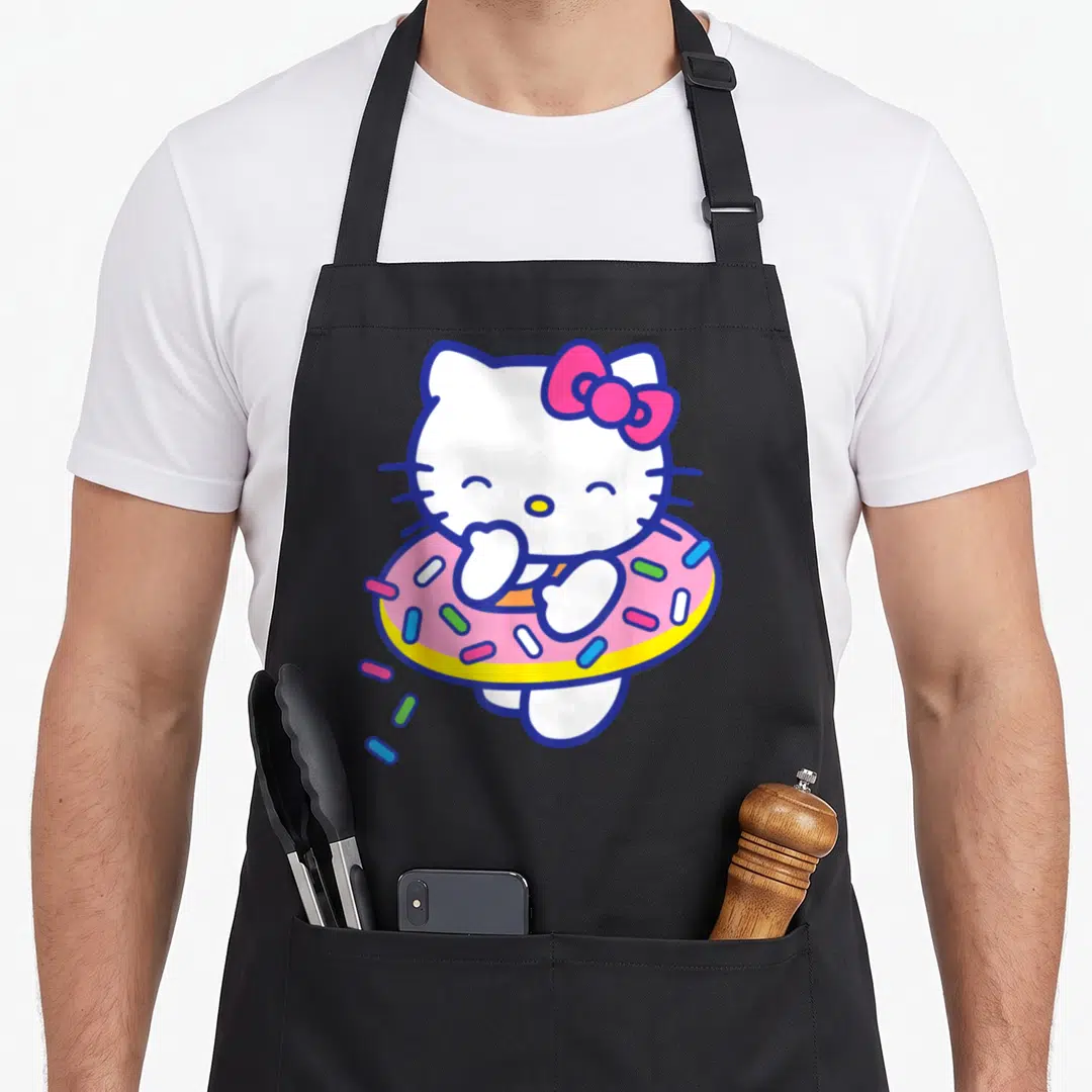 Sprinkle donut apron - Hello Kitty standing in a pink donut floaty with colorful sprinkles — shown on a black cotton canvas apron against a white background