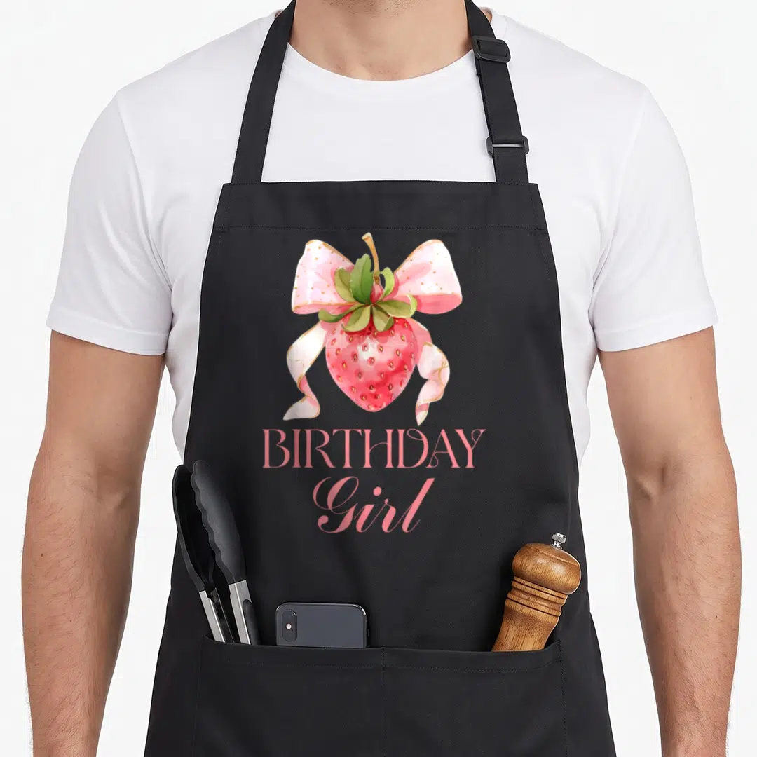 Bow strawberry apron - Watercolor red strawberry with pink polka-dot bow and BIRTHDAY Girl text — shown on a black cotton canvas apron against a white background