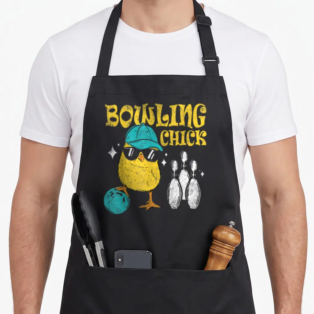 Chick bowl apron - Cartoon yellow chick with blue cap and sunglasses standing on a bowling ball near white pins — shown on a black cotton canvas apron against a white background
