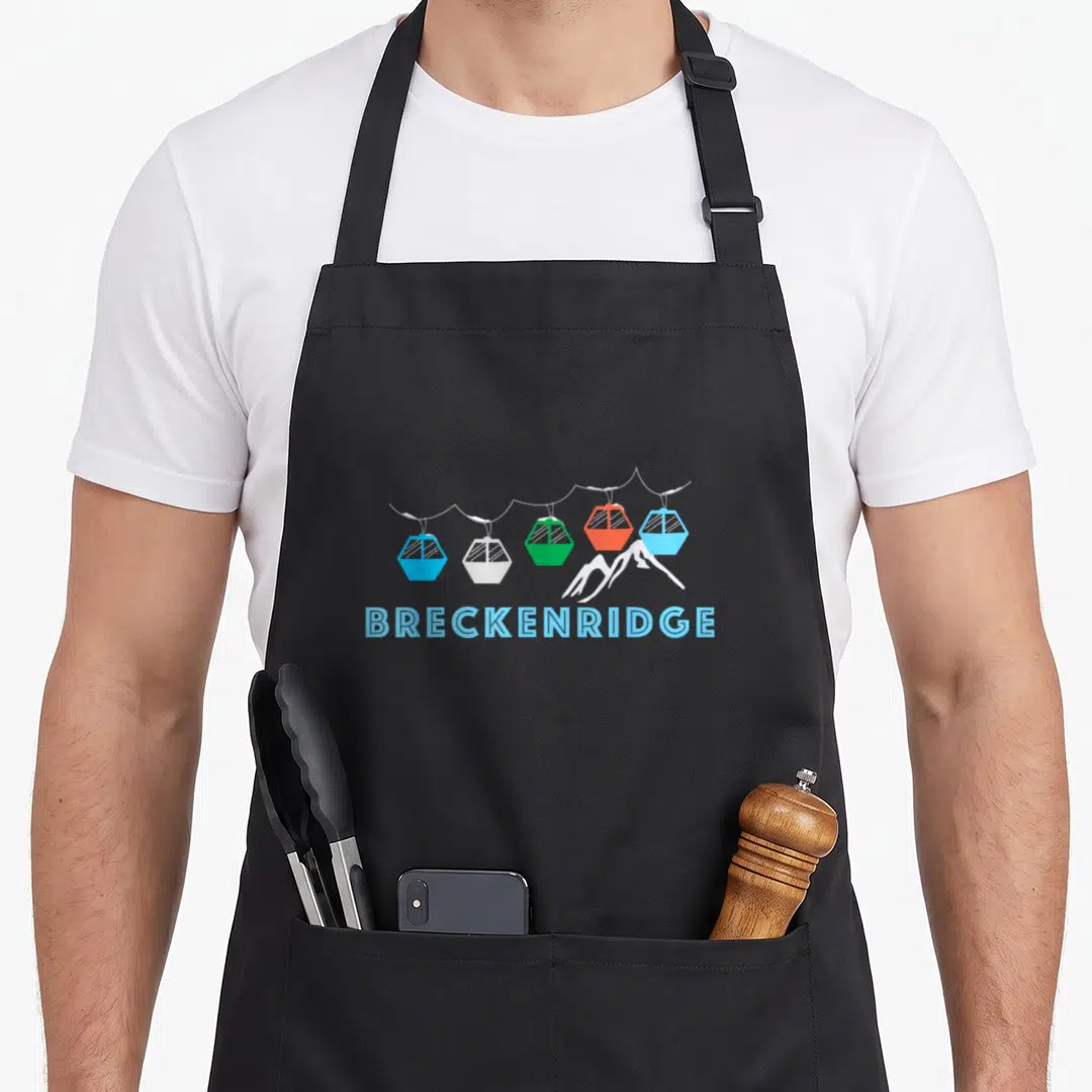 Breckenridge ski colorado apron - Five colorful gondolas on a cable above white peaks with BRECKENRIDGE text below — shown on a black cotton canvas apron against a white background
