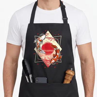 Japanese koi cherry apron - Two koi fish circling red sun in cream diamond frame with red petals — shown on a black cotton canvas apron against a white background