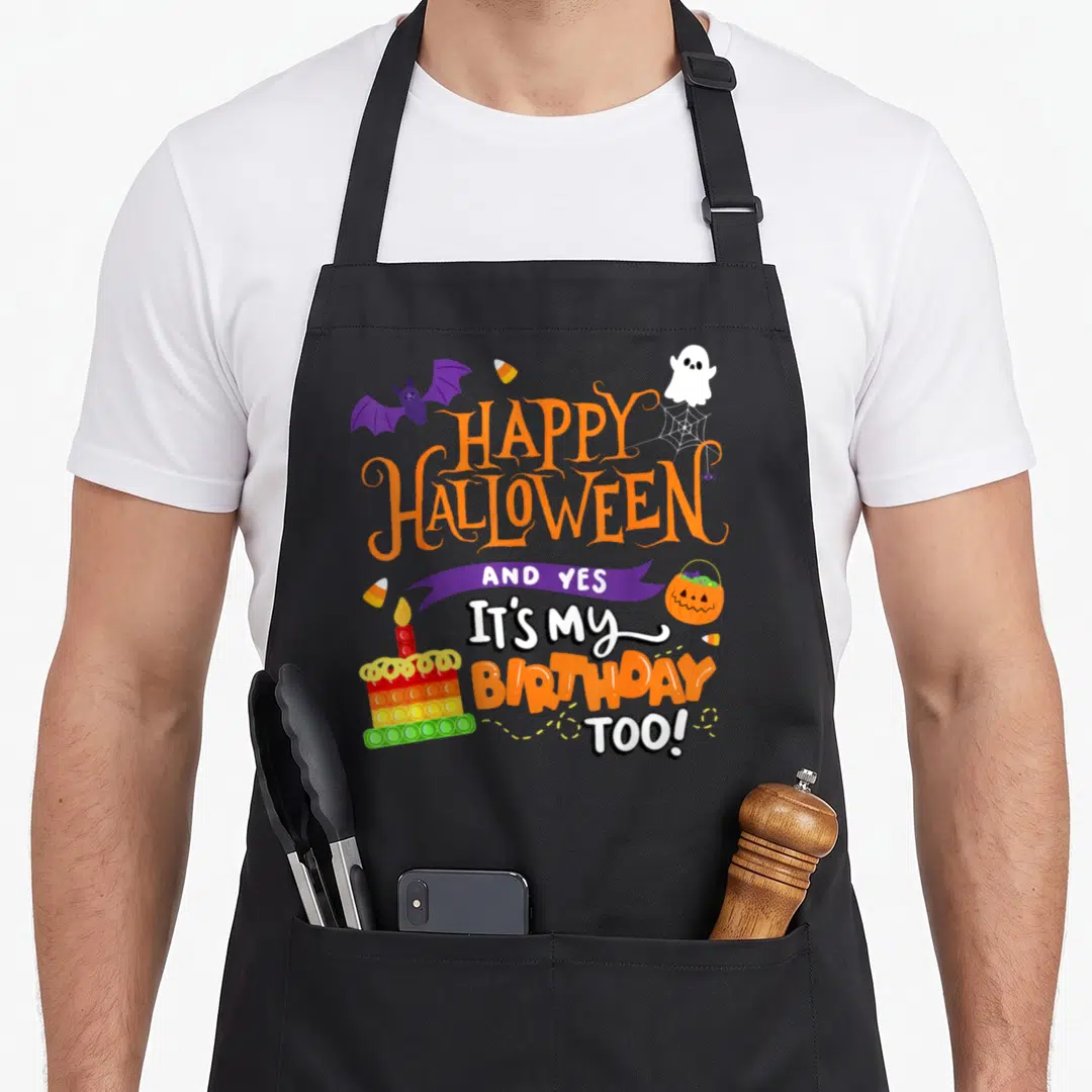 Cute birthday funny halloween apron - Stacked HAPPY HALLOWEEN birthday text with purple bat, white ghost, and rainbow — shown on a black cotton canvas apron against a white background