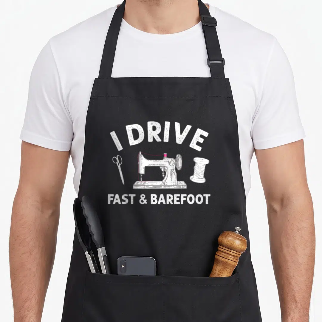 Sewer knitting apron - I Drive Fast & Barefoot text over white sewing machine with pink thread and scissors — shown on a black cotton canvas apron against a white background
