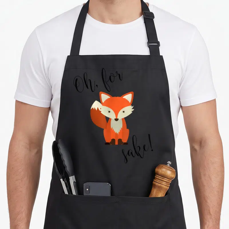 Sake fox print apron - Orange cartoon fox with Oh for sake text on black apron — shown on a black cotton canvas apron against a white background