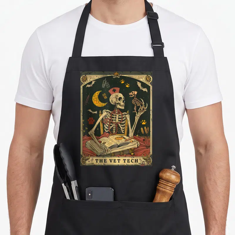 Vet skeleton apron - Skeletal nurse with stethoscope holds cat skeleton behind open book under crescent moon and bats — shown on a black cotton canvas apron against a white background