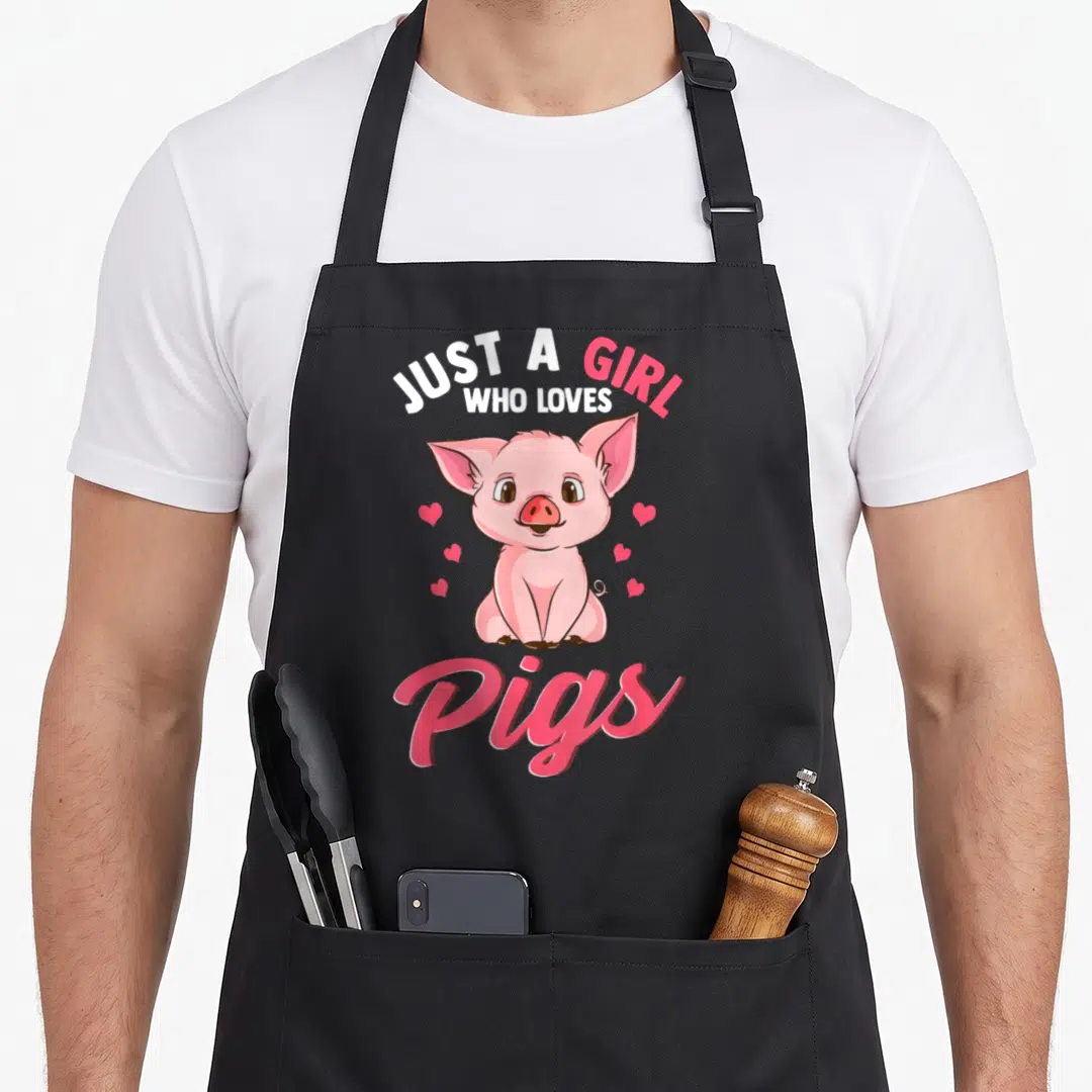 Hog farmer apron - Cartoon pink pig with arched text JUST A GIRL WHO LOVES Pigs and six hearts — shown on a black cotton canvas apron against a white background
